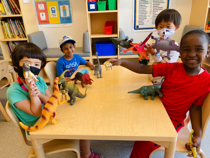 Four kindergarten students play with dinosaurs in the classroom